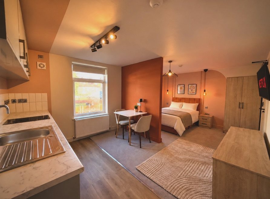 Studio apartment interior with orange accent walls, small dining area, and a bed.