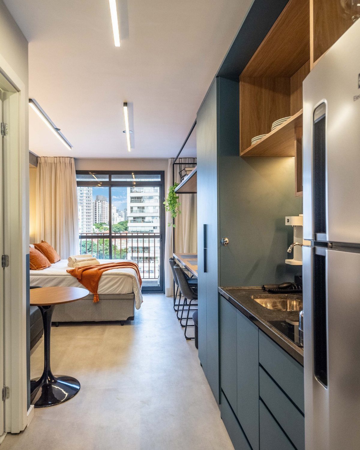 Studio apartment interior with a blue kitchenette and a bed near a balcony.