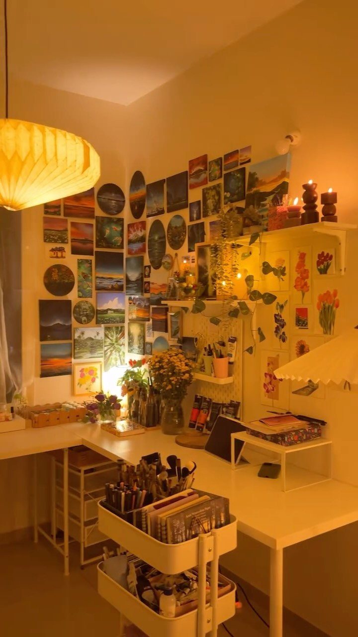 Wall covered in small landscape paintings above a white art desk and supplies.