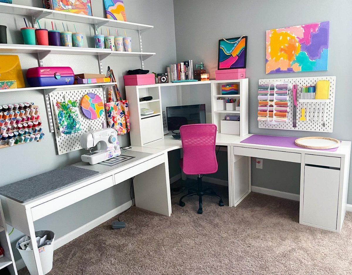 White L-shaped corner desk with a pink chair and colorful art supplies.