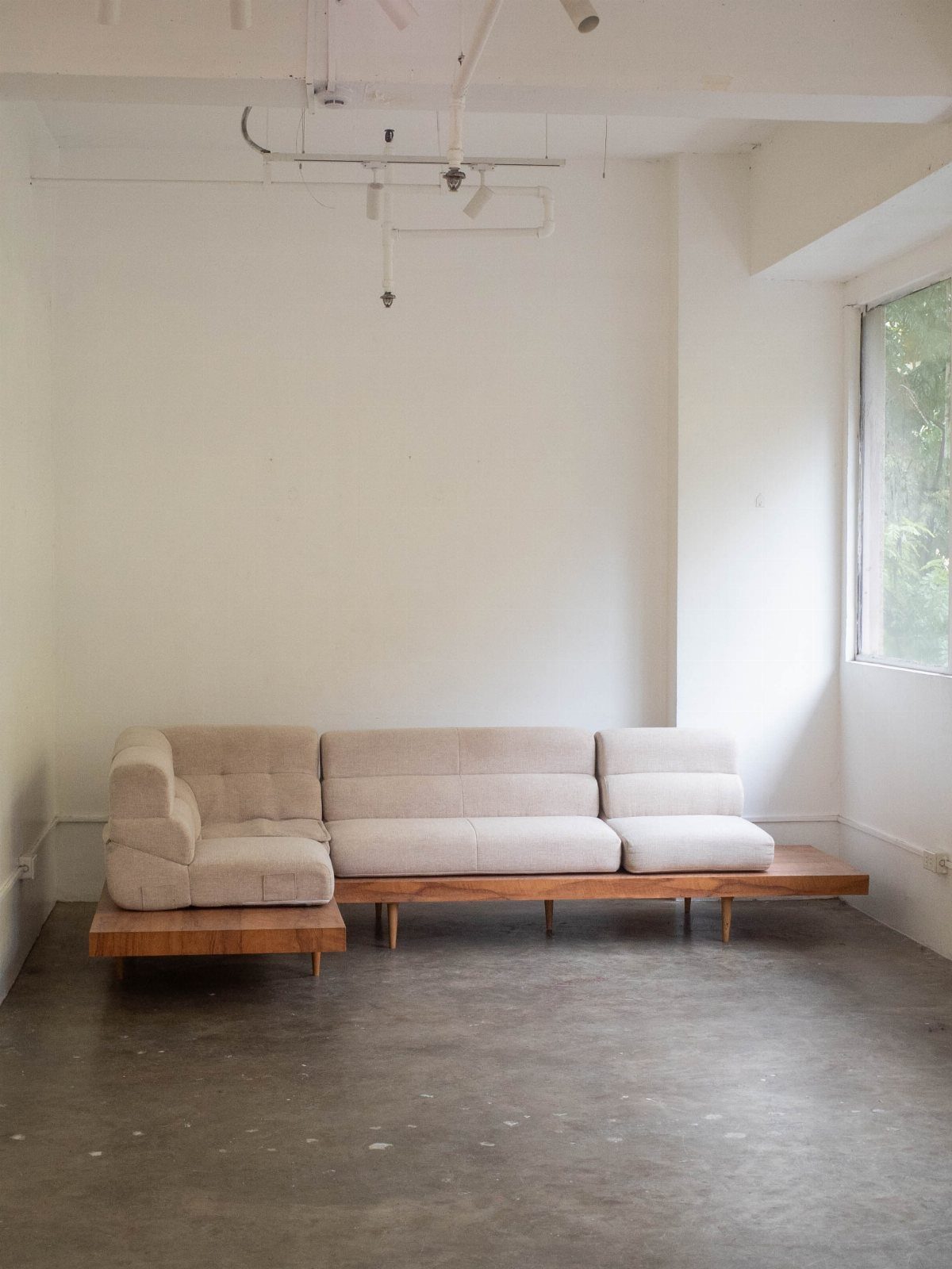 Beige modular sofa on a wooden platform in a minimalist white room