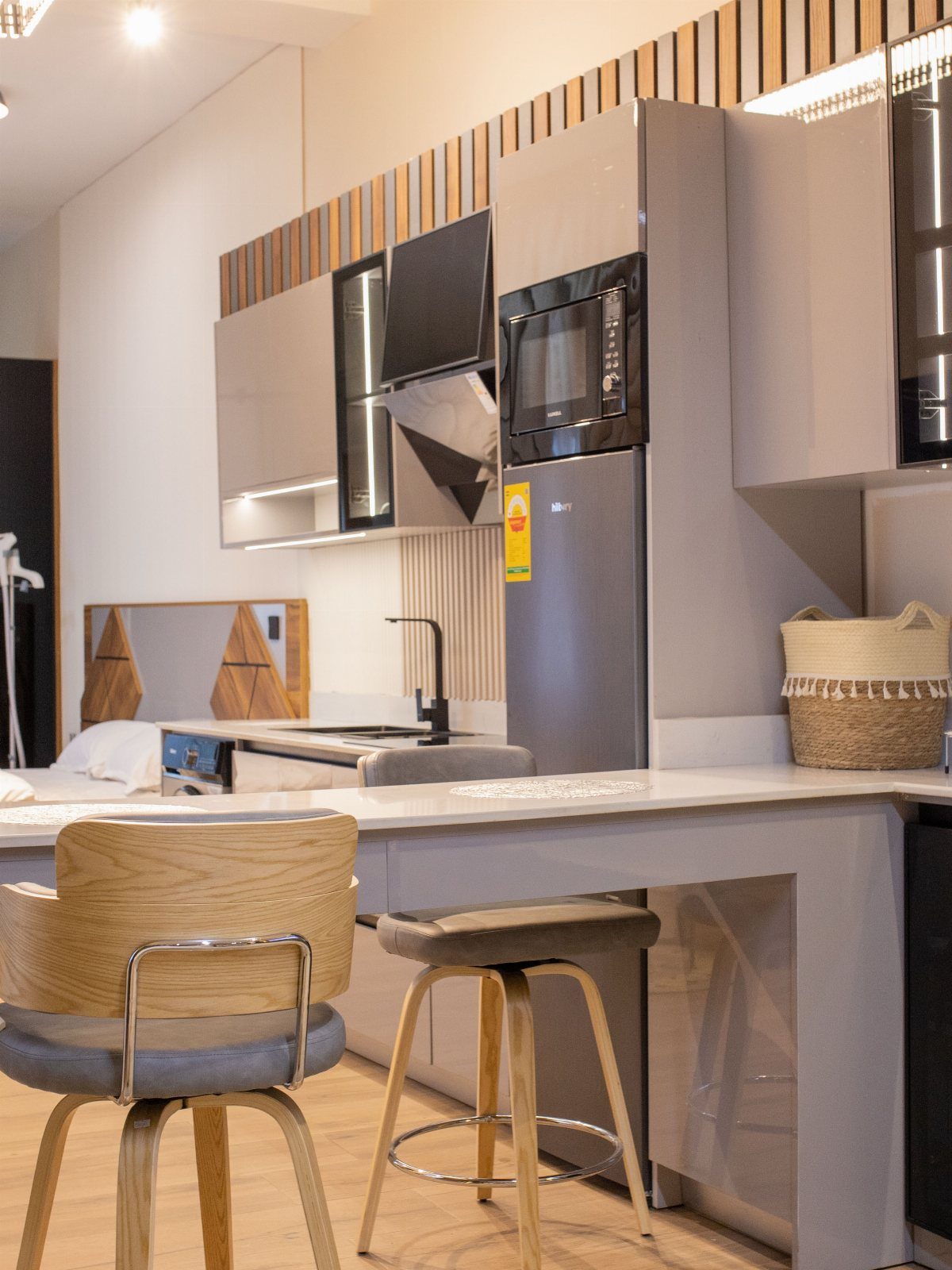 Modern studio kitchen with grey cabinets, white countertops, and wooden bar stools.