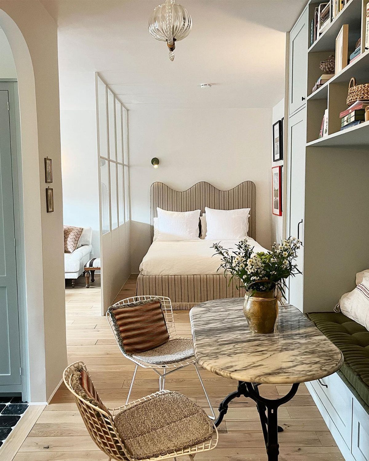 Studio apartment interior with a glass partition, marble table, and neutral color palette.