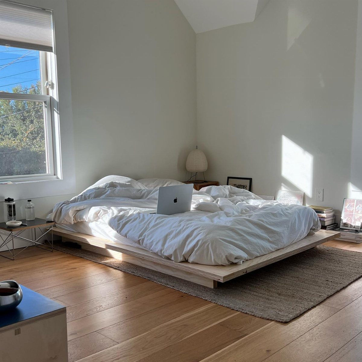 Low-profile wooden platform bed with white bedding in a bright, minimalist studio room.