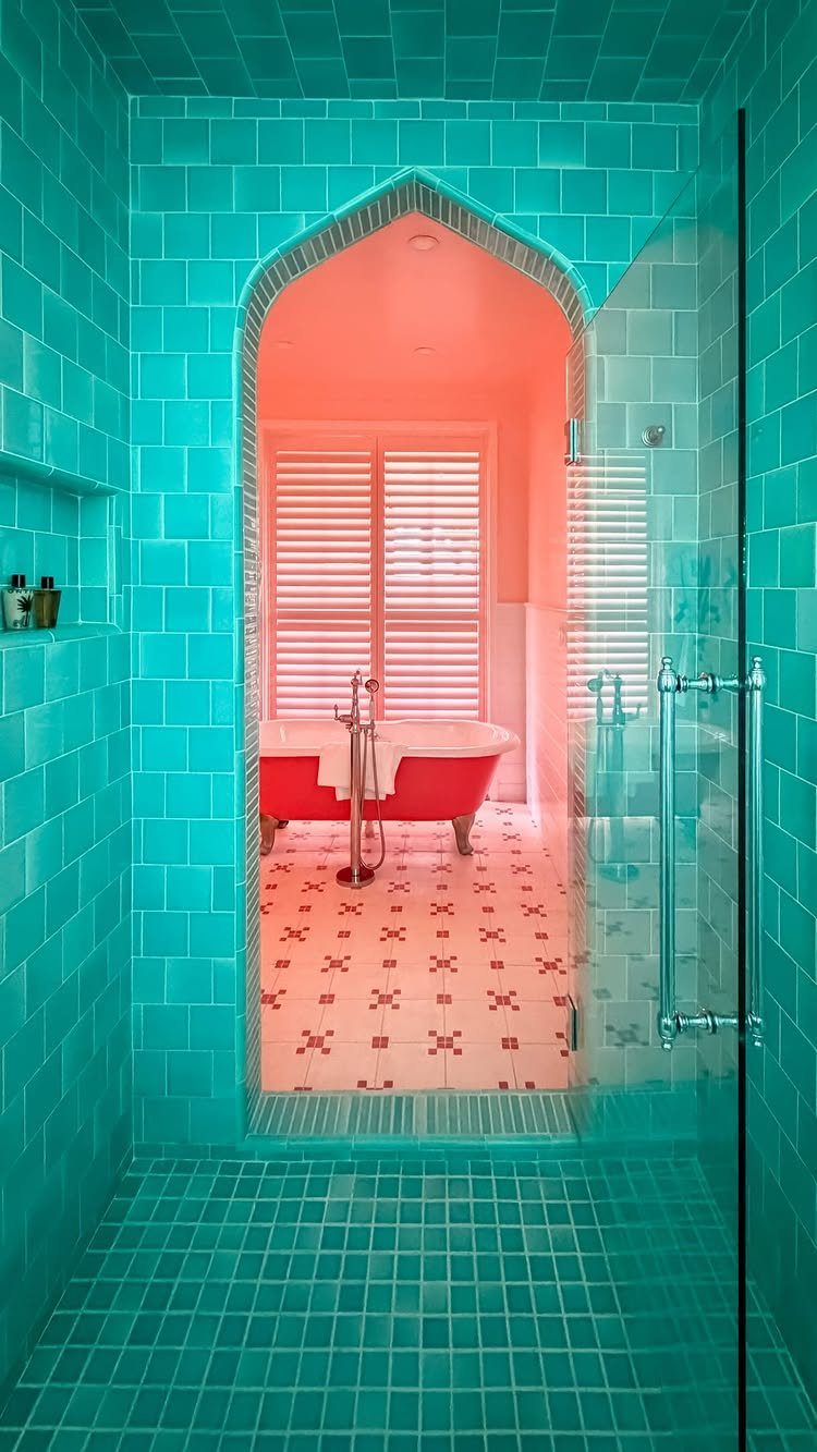 Turquoise tiled walk-in shower looking through an archway into a pink bathroom with tub.