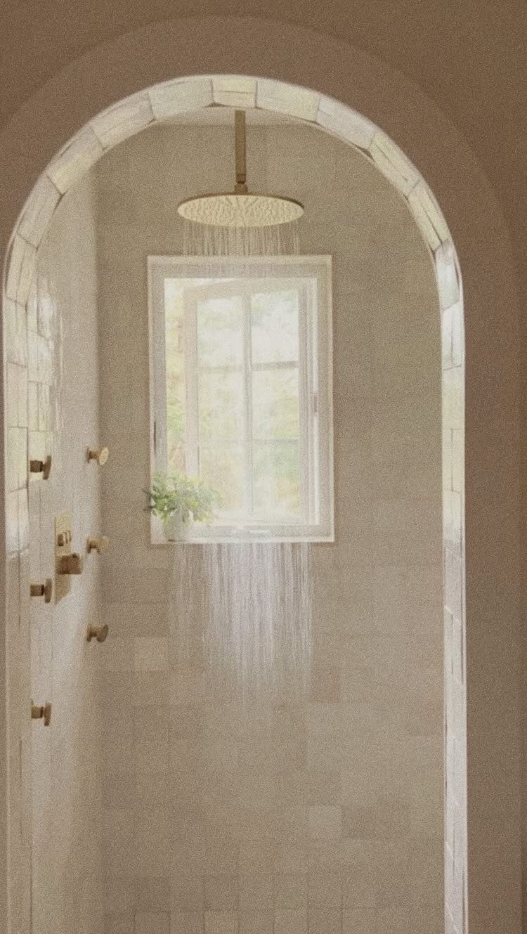 Arched walk-in shower with beige tiles, gold fixtures, and a rain showerhead.