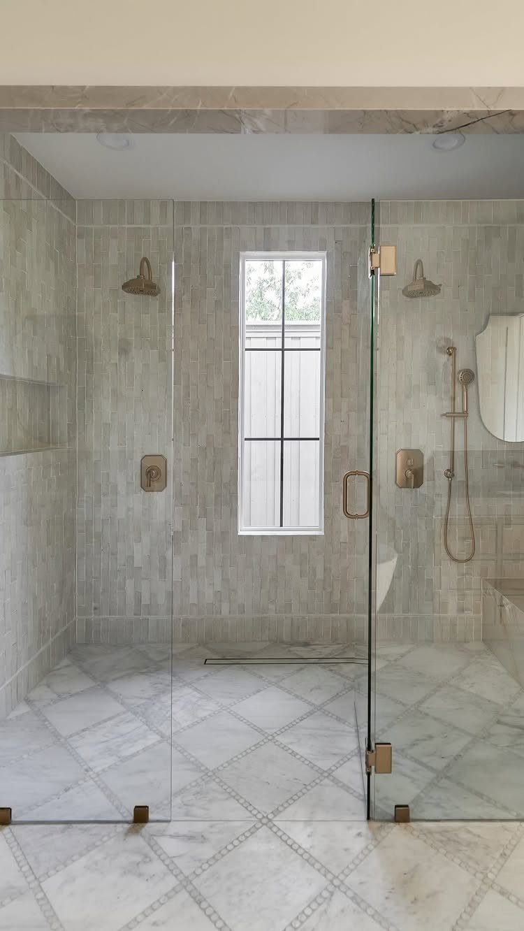 Frameless glass walk-in shower with grey tiled walls and marble diamond floor tiles.