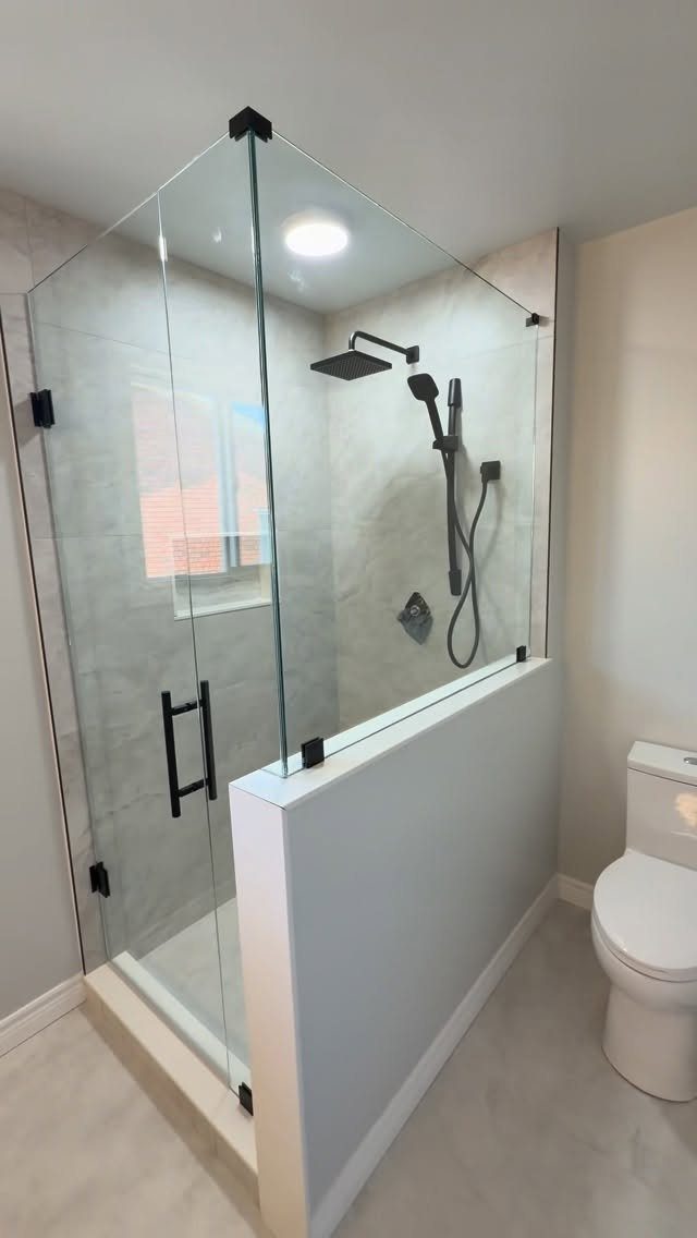 Walk-in shower with half-glass doors, matte black fixtures, and a white pony wall.