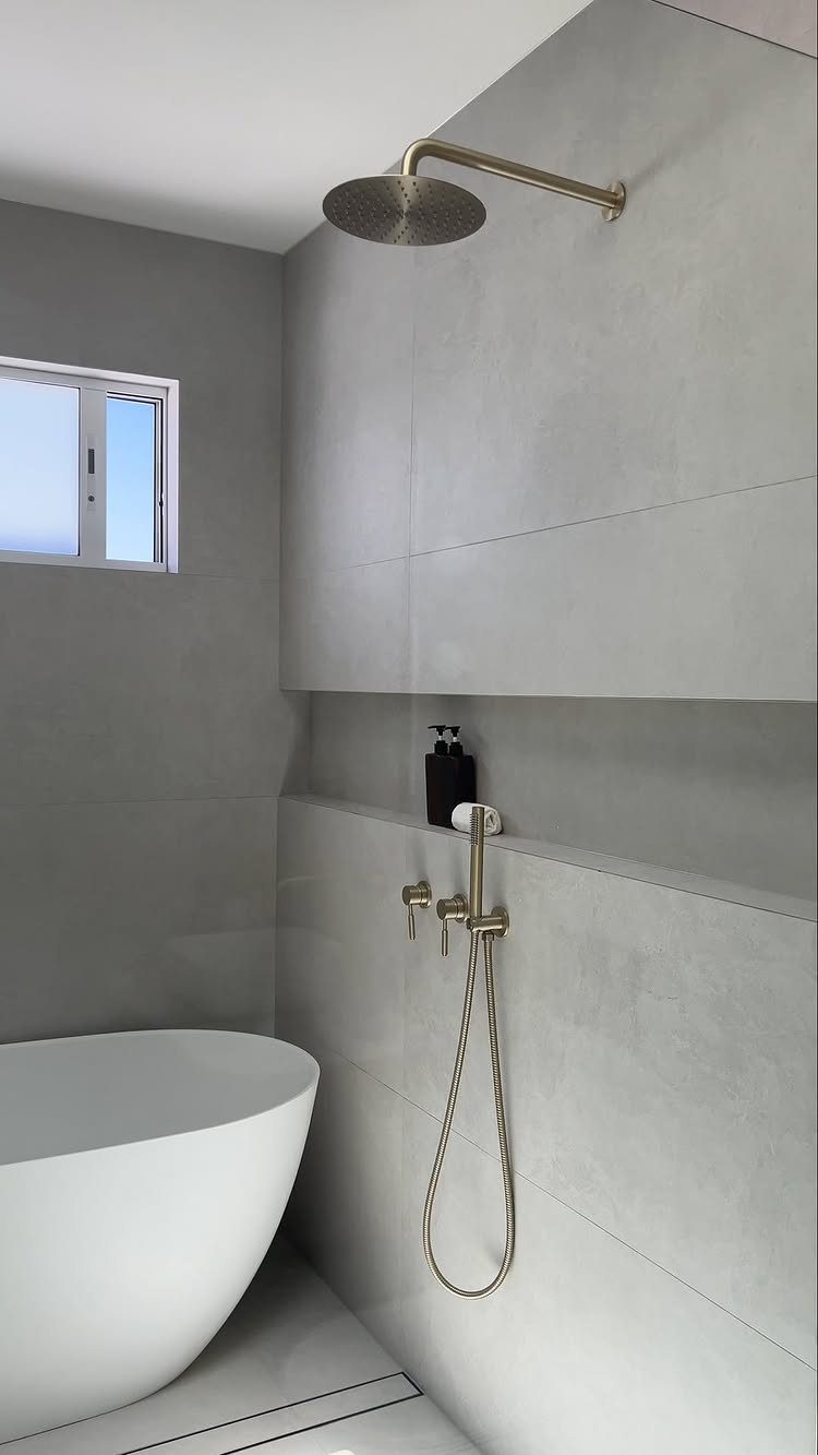Modern bathroom with white bathtub, grey tiles, and gold rain shower fixtures.