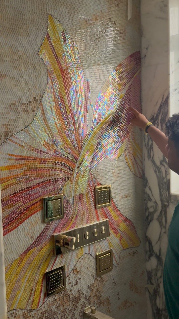 Colorful mosaic tile artwork on a shower wall with gold fixtures and a hand.