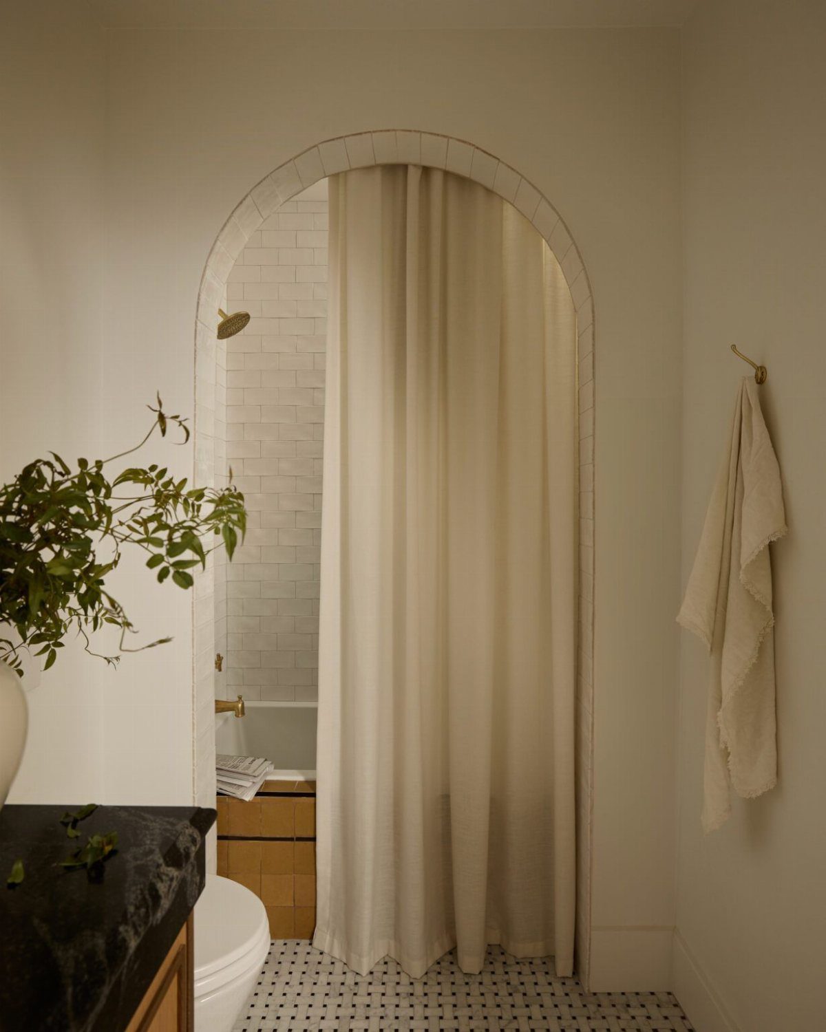 Cream fabric curtain hanging in an arched doorway of a white tiled shower
