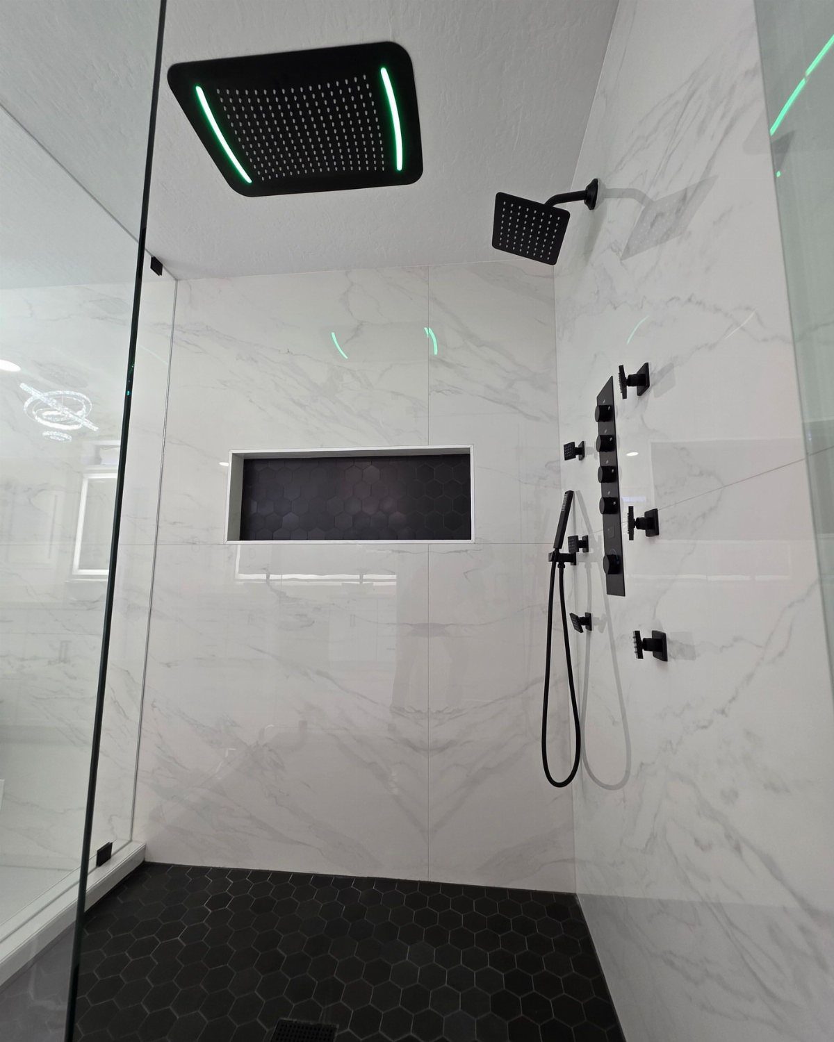 Modern shower with white marble walls, black hexagonal floor tiles, and black niche.