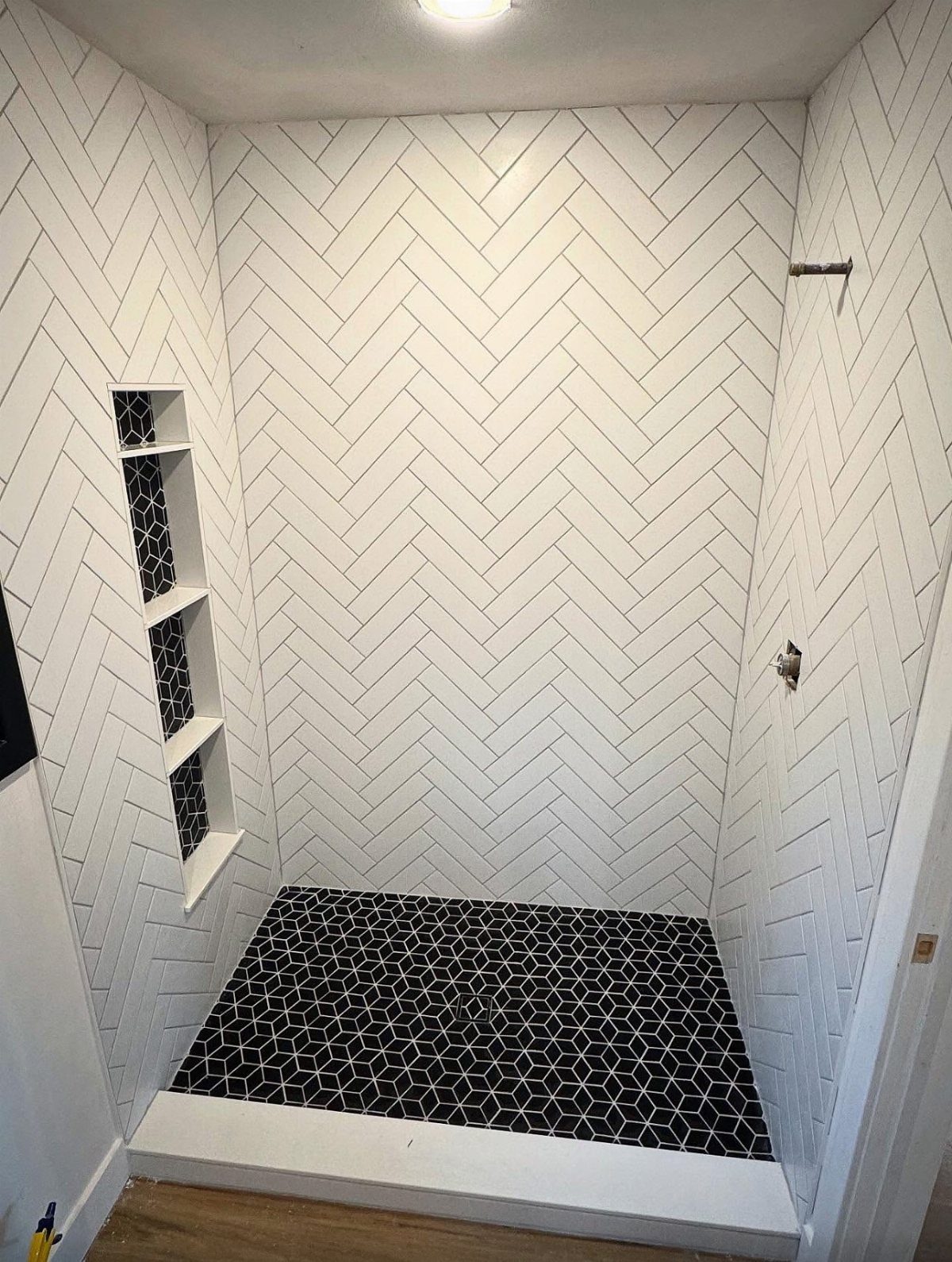 White herringbone wall tiles and black hexagonal floor tiles in a walk-in shower