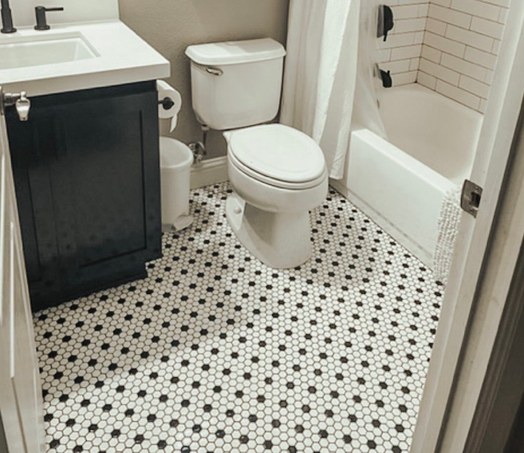 White and black penny tile bathroom floor with navy vanity and white toilet.