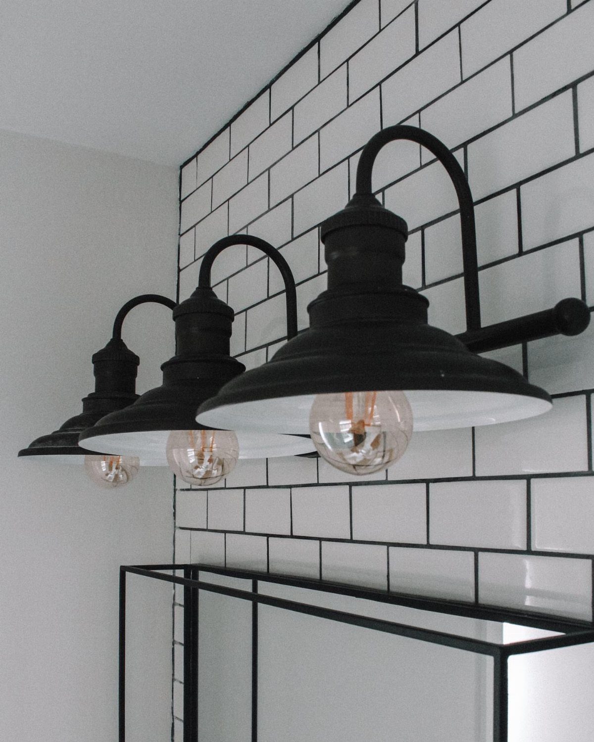 Black industrial wall lamps mounted on white subway tiles with black grout.
