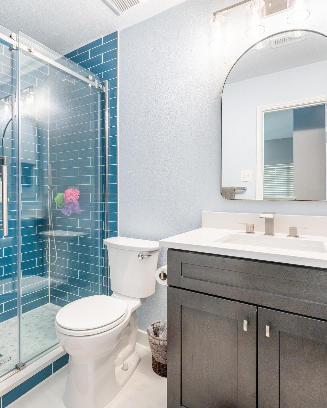 Blue vertical subway tiles in a shower next to a grey wood vanity.