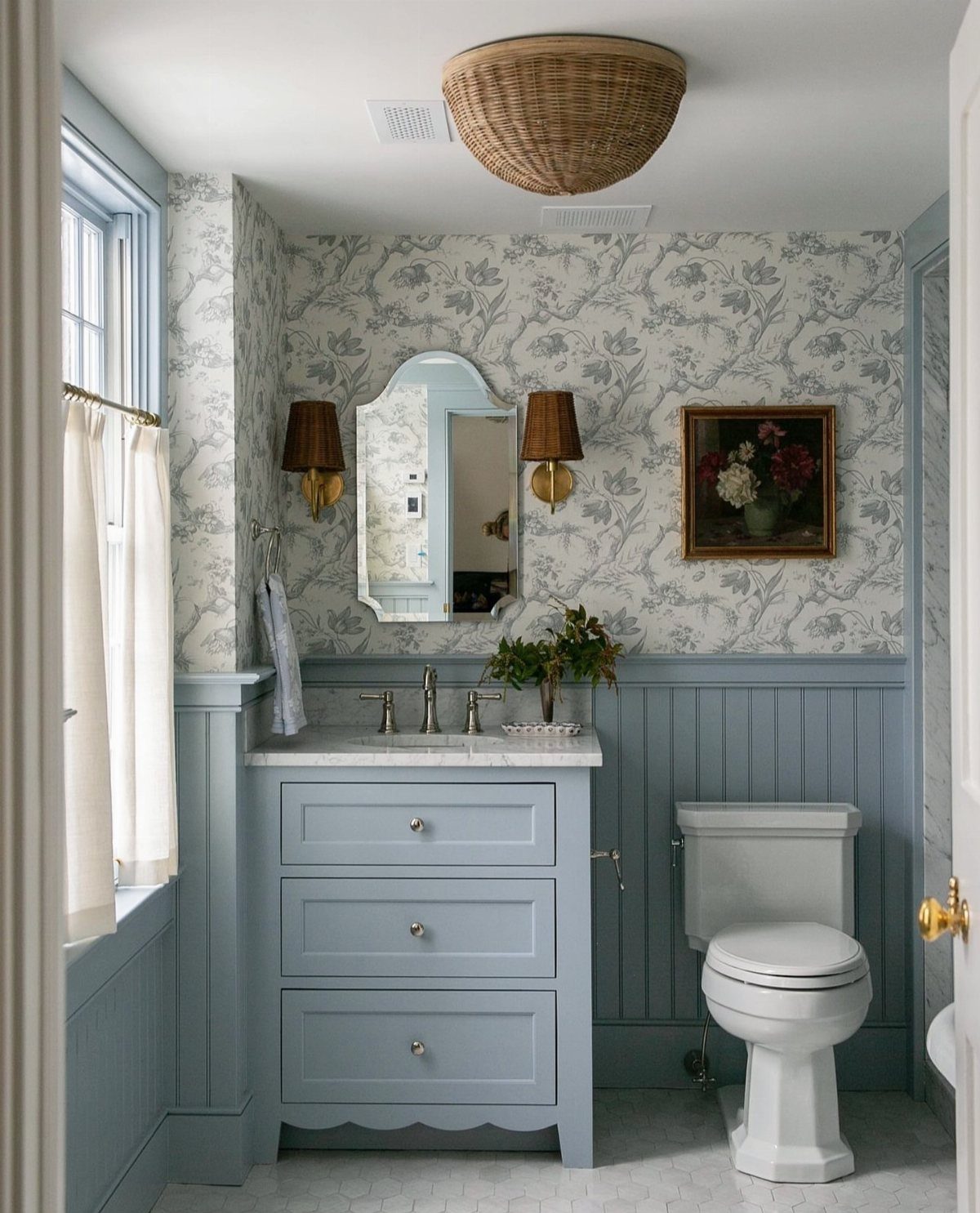 Light blue bathroom with floral wallpaper, blue vanity, and white toilet.