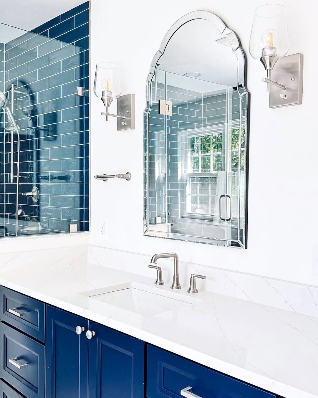Navy blue bathroom vanity with white marble countertop and blue subway tile shower.