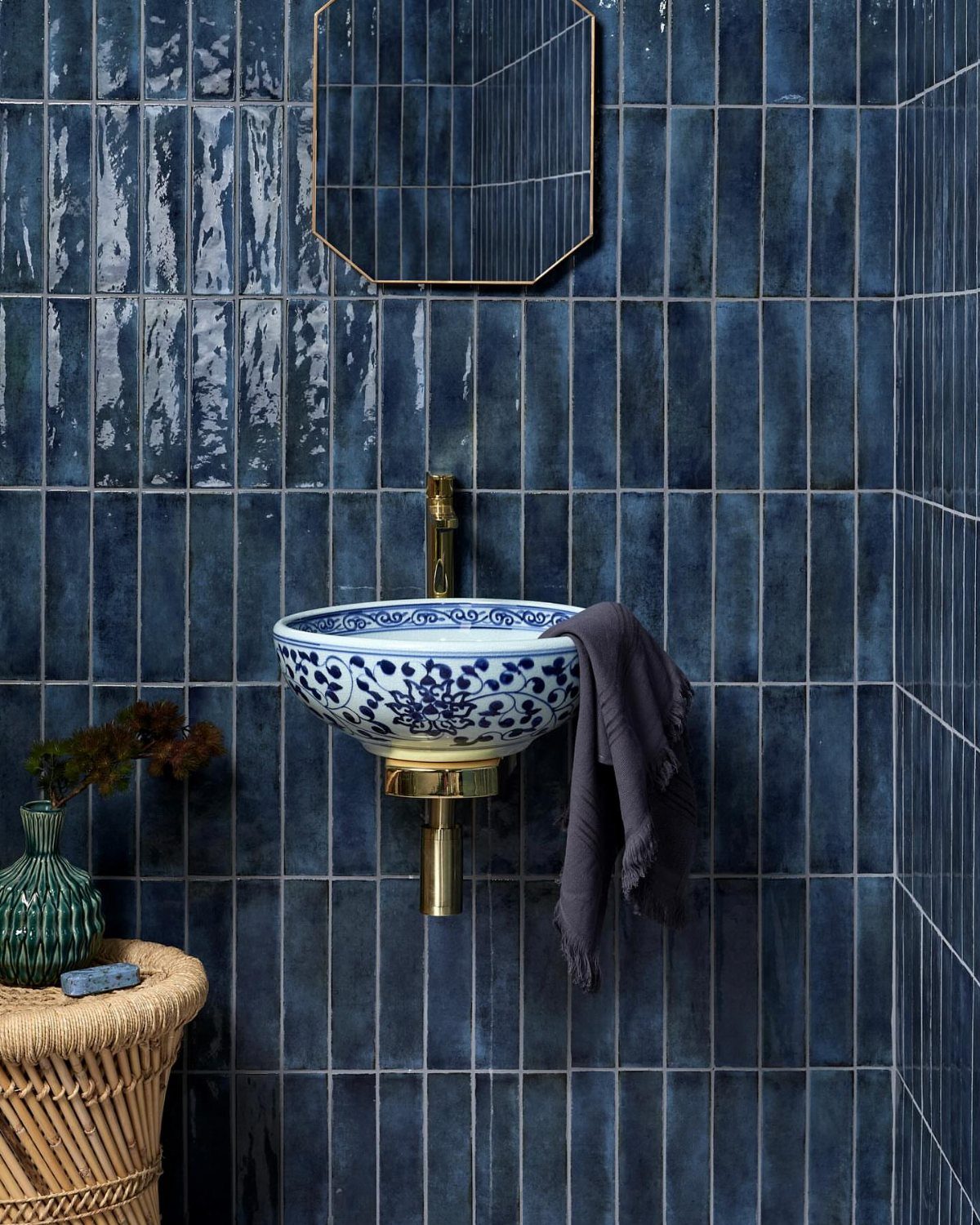 White and blue patterned vessel sink mounted on navy blue tiled bathroom walls.