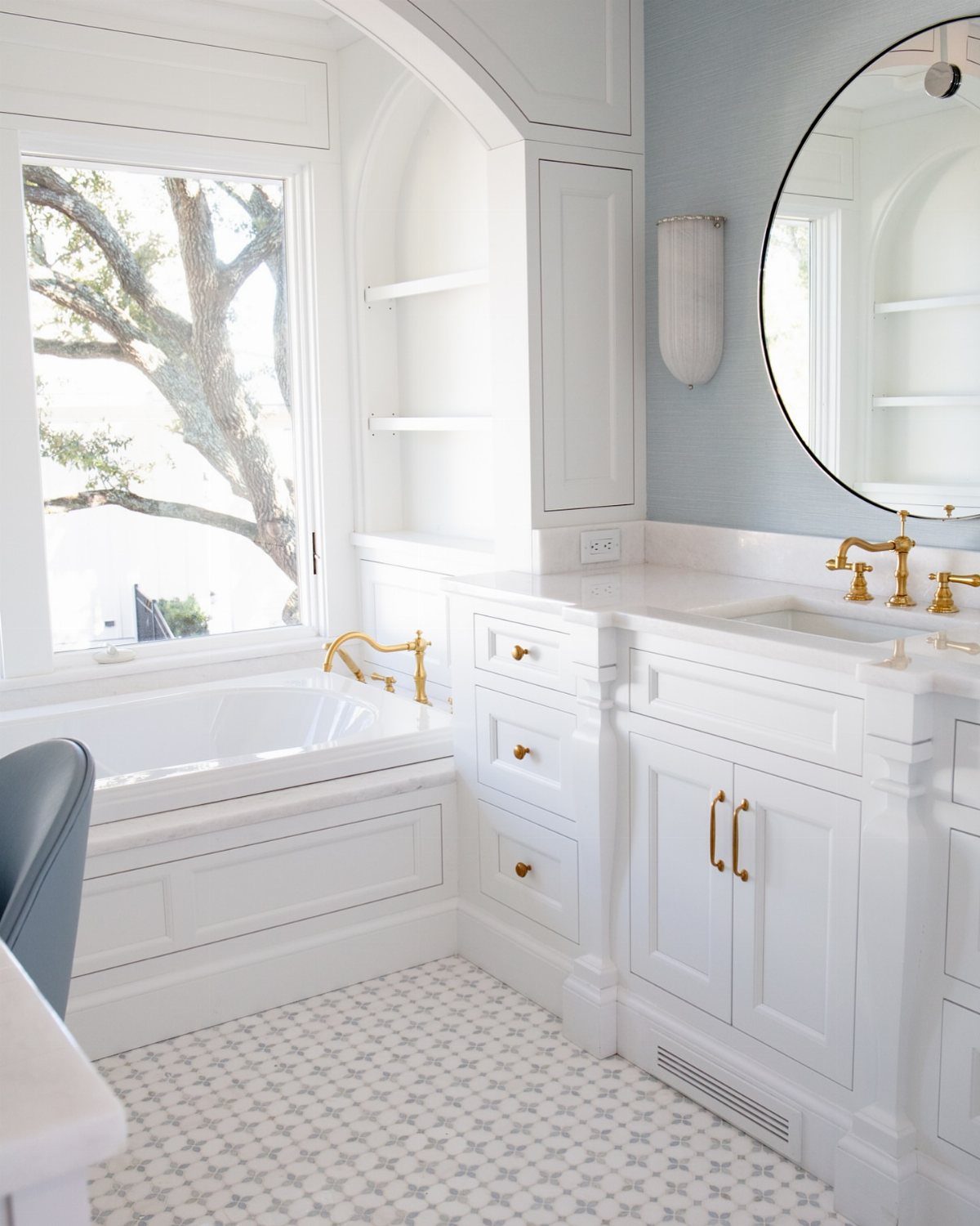 White bathroom vanity and bathtub against light blue walls with patterned tile flooring.