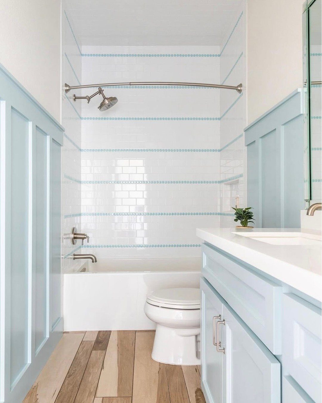 Light blue bathroom cabinetry and wainscoting paired with white walls and wood floors.